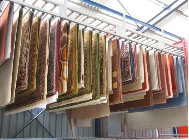 Tapetes de diferentes cores e estampas suspensos em uma estrutura de suporte.
